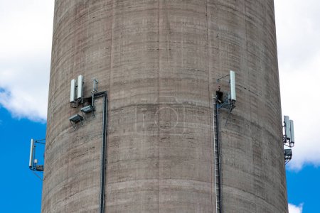 Foto de Un primer plano de las antenas de teléfono móvil instaladas en la pared de una chimenea de una planta de energía alta. Objeto contra el cielo azul en un día soleado. - Imagen libre de derechos