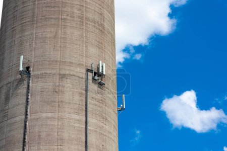 Téléchargez les photos : Gros plan des antennes de téléphonie mobile installées sur le mur d'une grande cheminée de centrale électrique. Objet contre le ciel bleu par une journée ensoleillée. - en image libre de droit