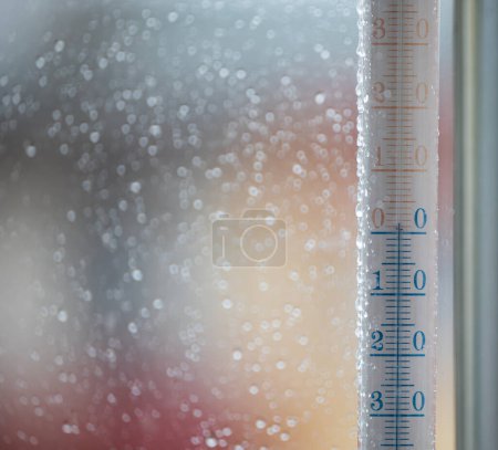 Téléchargez les photos : Un thermomètre à fenêtre indiquant la température extérieure. Gouttes de pluie sur le verre, fond flou devant la fenêtre - en image libre de droit