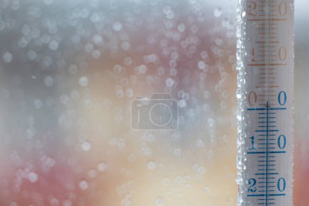 Téléchargez les photos : Un thermomètre à fenêtre indiquant la température extérieure. Gouttes de pluie sur le verre, fond flou devant la fenêtre - en image libre de droit
