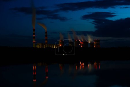 Foto de Vista nocturna de una central eléctrica de carbón. Las luces de la central eléctrica se reflejan en el lago. Altos costos de electricidad. Foto tomada por la noche con luz natural - Imagen libre de derechos