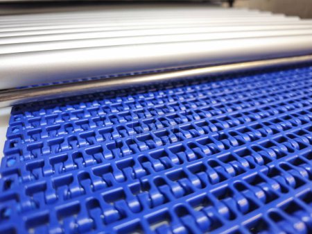 A close-up of a blue polyurethane belt in modular industrial conveyor system connected with roller conveyor. Transport systems in industrial factories.