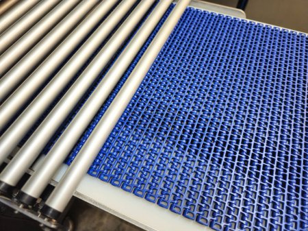 A close-up of a blue polyurethane belt in modular industrial conveyor system connected with roller conveyor. Transport systems in industrial factories.