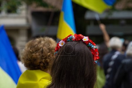 Closeup of a woman wearing a traditional Ukrainian head band Vinok with flowers and Ukrainian flags on the background
