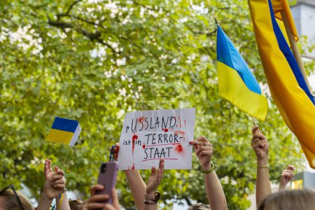 Photo for Ukrainian flags and hands holding sign that says Russia is a terrorist state - Royalty Free Image