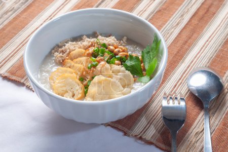 Bubur Ayam Sukabumi contains white rice porridge with side dishes of fried chicken slices, fried soybeans, emping crackers and sprinkled with fried onions and celery