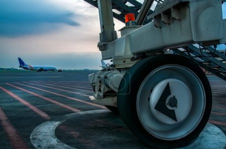 Téléchargez les photos : Gros plan des roues du jetway sur l'aire de trafic de l'aéroport avec un avion décollant en arrière-plan - en image libre de droit