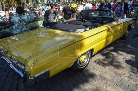 Téléchargez les photos : Les personnes inspectant Classic vintage jaune voiture américaine Buick Electra 225 Convertible 1962 à l'exposition de voitures rétro - en image libre de droit