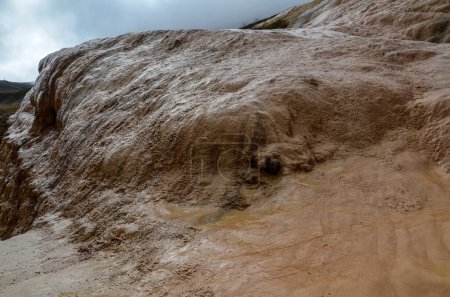 L'eau coule à travers une surface texturée de dépôts minéraux multicouches dans diverses nuances de brun et de beige. Travertin Jvari Pass, texture naturelle ou fond