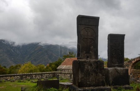 The stone adorned with intricate designs called khachkar or Armenian carved cross-stone stands on the territory of the Odzun Church against a backdrop of misty mountains and cloudy sky