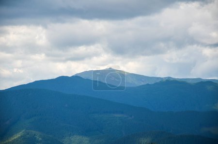 A serene and captivating landscape showcasing the majestic beauty of a mountain range with highest peak Pip Ivan with observatory enveloped in the soft embrace of cloudy skies. Carpathians, Ukraine