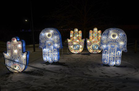 Photo for Illuminated artistic installations shaped like hands and Hamsa symbols, adorned with intricate designs, glowing against the backdrop of a dark snowy landscape - Royalty Free Image