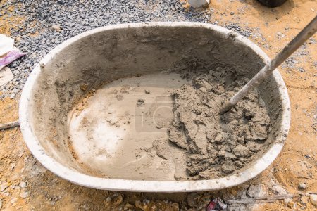Foto de Mezclar arena de cemento y piedras con fugas de azada dentro de un gran cubo en el fondo del suelo - Imagen libre de derechos