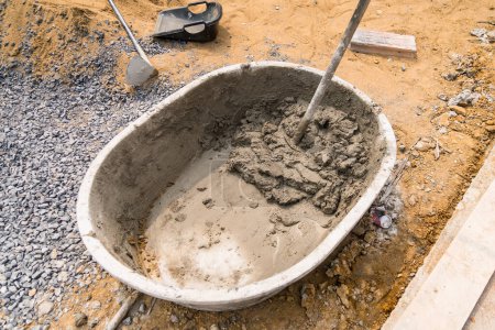 Foto de Mezclar arena de cemento y piedras con fugas de azada dentro de un gran cubo en el fondo del suelo - Imagen libre de derechos