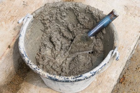 Téléchargez les photos : Mélanger le sable de ciment et les pierres avec la fuite de houe à l'intérieur grand seau sur fond de plancher - en image libre de droit