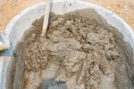 Téléchargez les photos : Mélanger le sable de ciment et les pierres avec la fuite de houe à l'intérieur grand seau sur fond de plancher - en image libre de droit