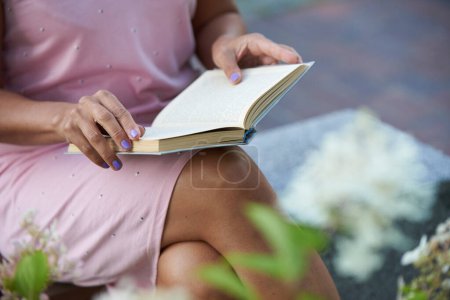 Frau im rosa Kleid liest auf einer Bank draußen ein Buch