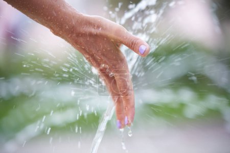 A woman's hand under splashes of water from a fountai