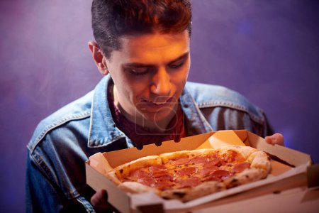 Young happy guy with pepperoni pizza in a cardboard box.