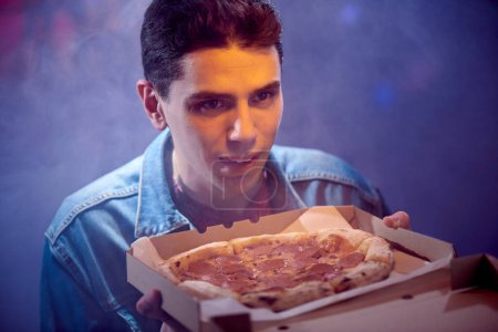 Young happy guy with pepperoni pizza in a cardboard box.
