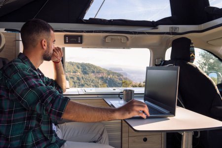 jeune homme travaillant sur son ordinateur portable depuis son camping-car au milieu de la nature, concept de liberté et mode de vie numérique nomade