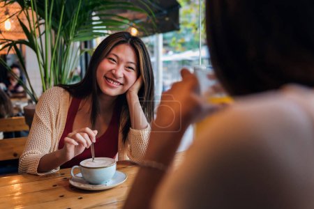 Téléchargez les photos : Young asian woman smiling in love to her friend during their date in a coffee shop, concept of friendship and love between women - en image libre de droit