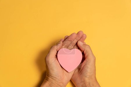 Foto de Papel rosa corazón en la mano sobre fondo amarillo - Imagen libre de derechos
