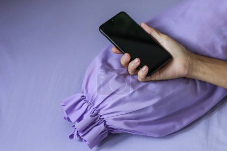 Photo for A black smartphone in man hand on purple bed - Royalty Free Image