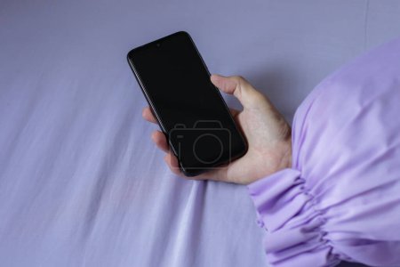 Foto de Un teléfono inteligente negro en la mano del hombre en la cama púrpura - Imagen libre de derechos