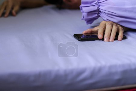 Foto de Un teléfono inteligente negro en la mano del hombre en la cama púrpura - Imagen libre de derechos