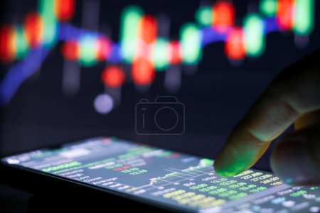 Photo for Businessman finger touching screen on smartphone with stock market graph at night. - Royalty Free Image