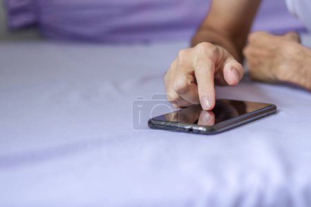 Téléchargez les photos : Homme utilisant un smartphone noir sur lit violet - en image libre de droit