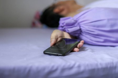 Téléchargez les photos : Un smartphone noir à la main sur lit violet - en image libre de droit