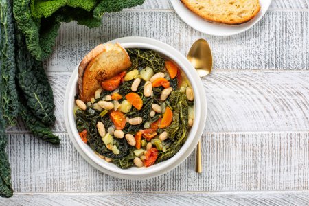 Top view of Ribollita. Tuscan bread soup made with toasted bread and vegetables. Cannellini beans, lacinato kale, cabbage verza, carrot, celery, potatoes, and onion. Itralian food. Directly above.