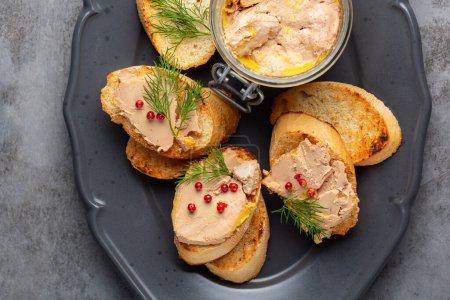 Téléchargez les photos : Bread or baguette toast with foie gras pate, directly above. A specialty food product made of the liver of a duck or goose,  in a glass jar. Decorated with red pepper and dill. - en image libre de droit