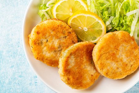 Photo for Top view of Fish cakes or burger, or cutlets. Made from ground perch and tuna with herbs, breaded and fried, served with iceberg salad, lemon slices. - Royalty Free Image