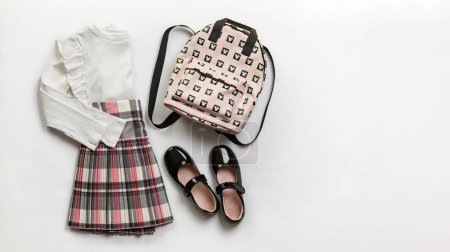 Photo for Girls clothes,  primary or elementary school uniform, white blouse and plaid skirt, black shoes, backpack on white background.  Copy space. - Royalty Free Image