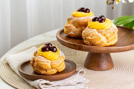Foto de Table with Italian pastry - zeppole di San Giuseppe - baked puffs made from choux pastry, filled and decorated with custard cream and cherry.  Saint Joseph's Day. - Imagen libre de derechos