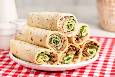 Photo for Piadina or piada, thin Italian flatbread rollups, typically prepared in the Romagna, rolled with feeling, ground meat, mushrooms, cream cheese, rocket salad or arugula.  Italian food. - Royalty Free Image