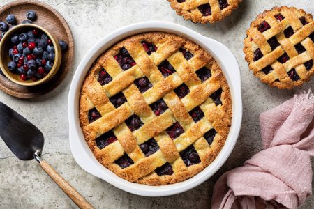 Photo for Whole baked mixed berry crust pie or tart with lattice, and mini tarts. Homemade, fresh berries. Light table surface, directly above. - Royalty Free Image