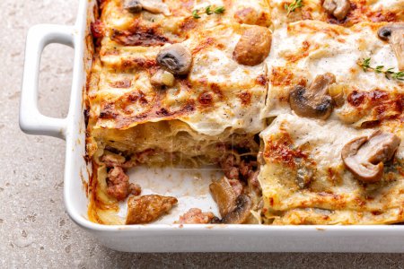 Close-up of homemade casserole with white lasagna with porcini and champignon mushrooms, onion and sausages. Pasta with parmesan cheese and bechamel sauce.