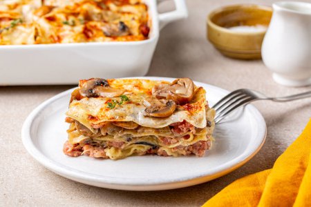 Téléchargez les photos : Trancher des lasagnes blanches maison savoureuses avec des porcini et des champignons champignon, oignon et saucisses de viande. Pâtes au parmesan et sauce bechamel. - en image libre de droit