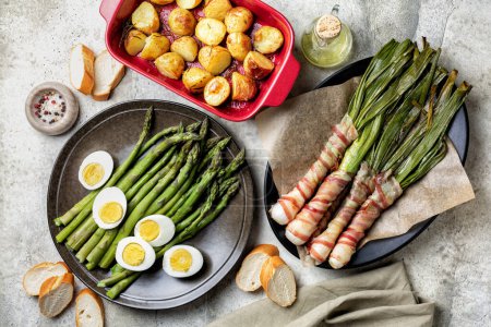 Photo for Spring dish green asparagus with hard boiled eggs, sicilian bacon wrapped scallions or spring onions, baked in oven, oven-roasted new potatoes. Homemade simple food concept. Top view. - Royalty Free Image