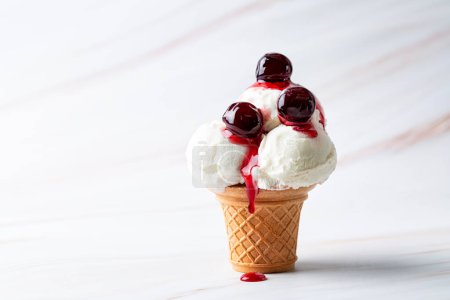Téléchargez les photos : Cuillère de crème glacée vanille dans un cône de gaufre de service avec des cerises en conserve et du sirop de cerise sur fond blanc, espace de copie. - en image libre de droit