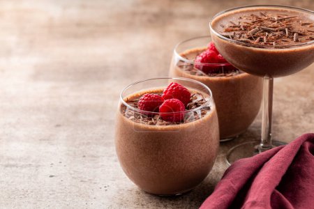 Photo for Homemade chocolate mousse decorated with raspberries and dark chocolate sprinkles in portion glasses. Brown table. Selective focus, copy space. - Royalty Free Image