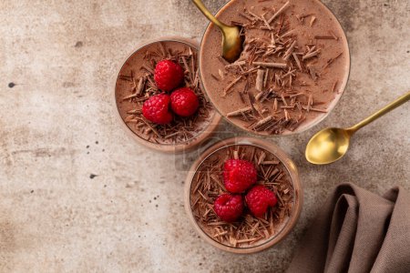Photo for Flat lay with chocolate mousse or pudding decorated with raspberries and dark chocolate sprinkles in portion glasses. Brown table. Copy space. - Royalty Free Image