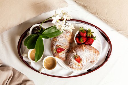 Photo for Top view of Breakfast in the bed of a bedroom. Two cups of coffee for a couple, croissant with cream and strawberries. White flowers. Romantic concept. - Royalty Free Image