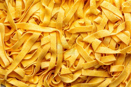 Homemade fresh, uncooked tagliatelle or fettuccine background, traditional type of Italian pasta. Long, flat ribbons traditionally made of egg and flour. Directly above.