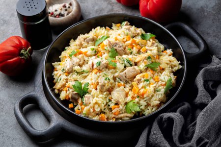 Poulet Pilaf, pilau ou biryani. Plat à base de riz à grains longs, viande et légumes de poulet, oignon, carottes, épices et persil. Cuisine orientale. Fond gris foncé.