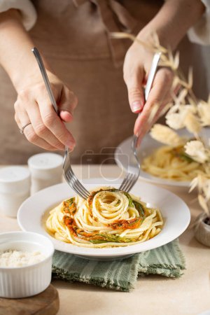 Téléchargez les photos : Une femme qui sert des pâtes italiennes, des spaghettis aux fleurs de courgettes, du poivre noir et du fromage. Mains à la fourchette. Image verticale. - en image libre de droit